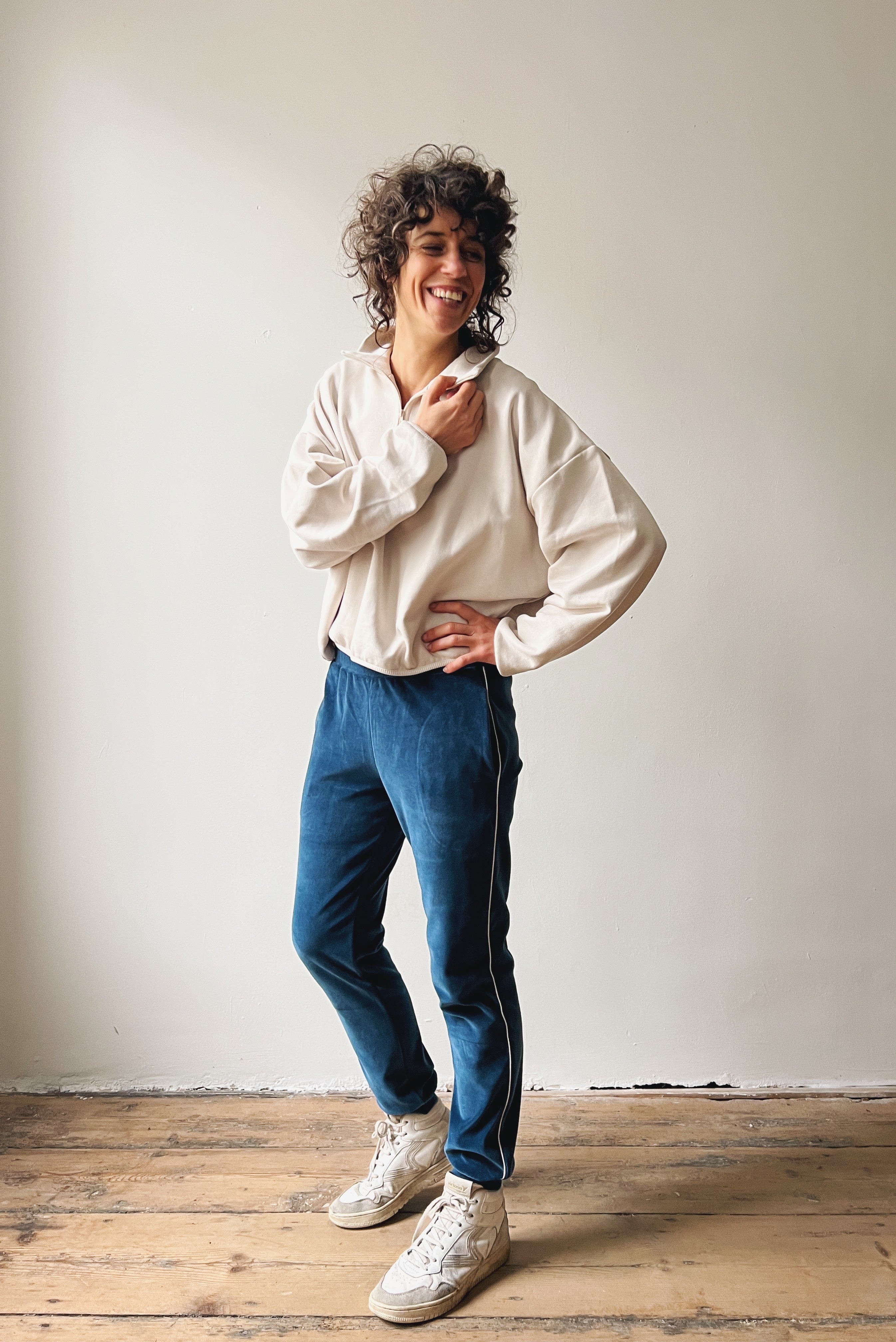 Woman wearing an oversized white sweater, ocean blue velvet sweatpants and white sneakers.