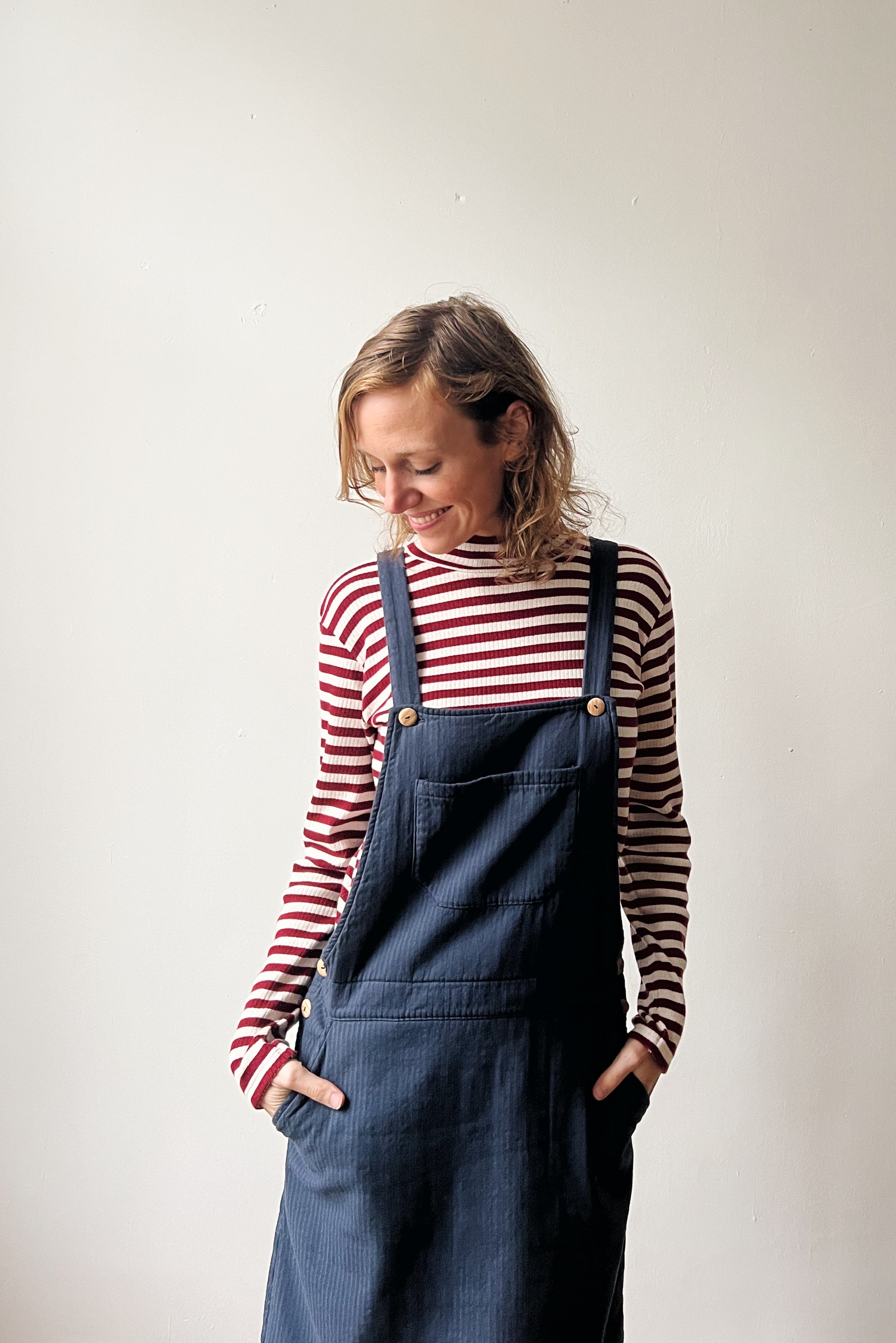 Person wearing a red and white turtleneck and corduroy salopettedress against a plain background