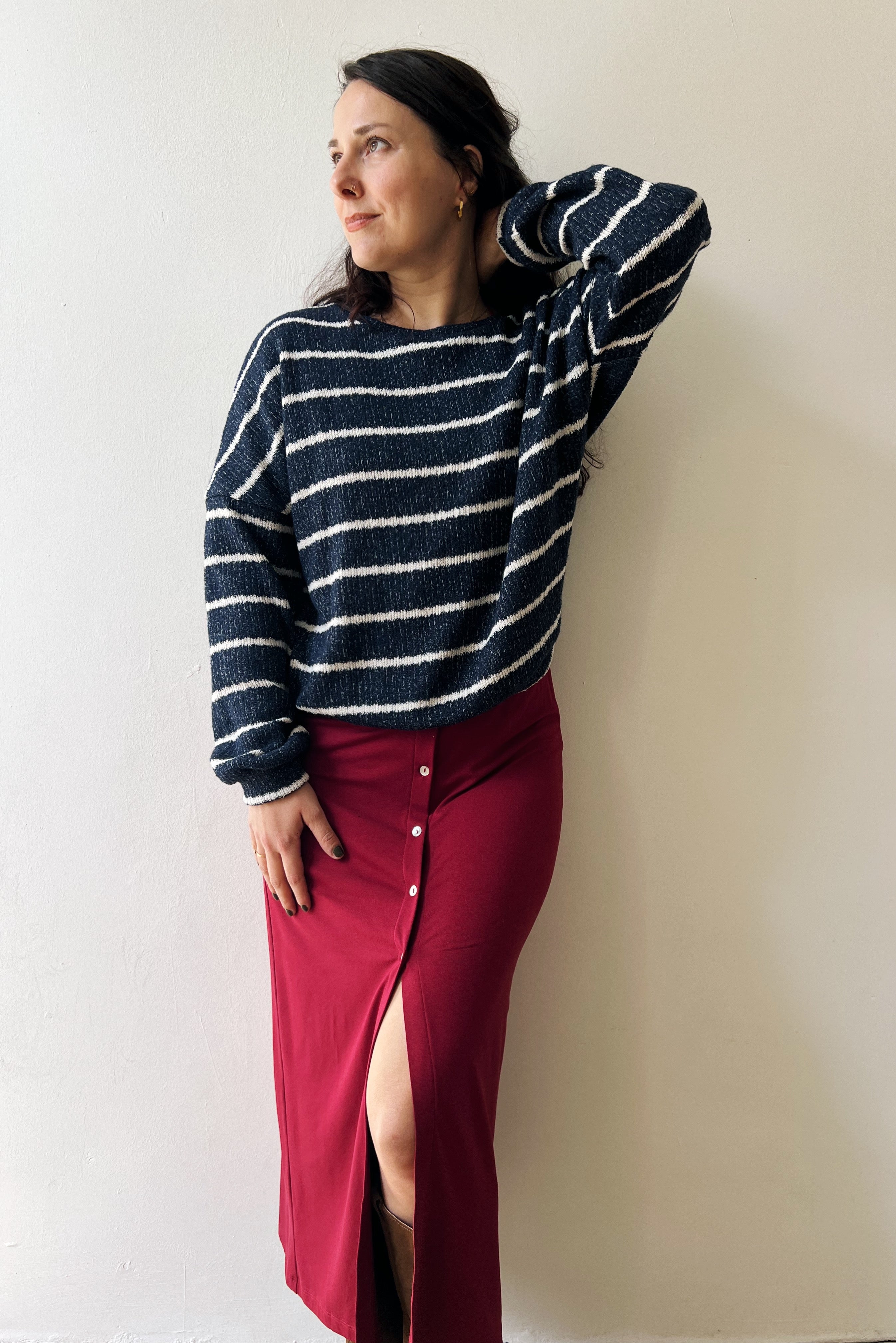 Woman wearing a navy and white striped sweater and red skirt against a plain background