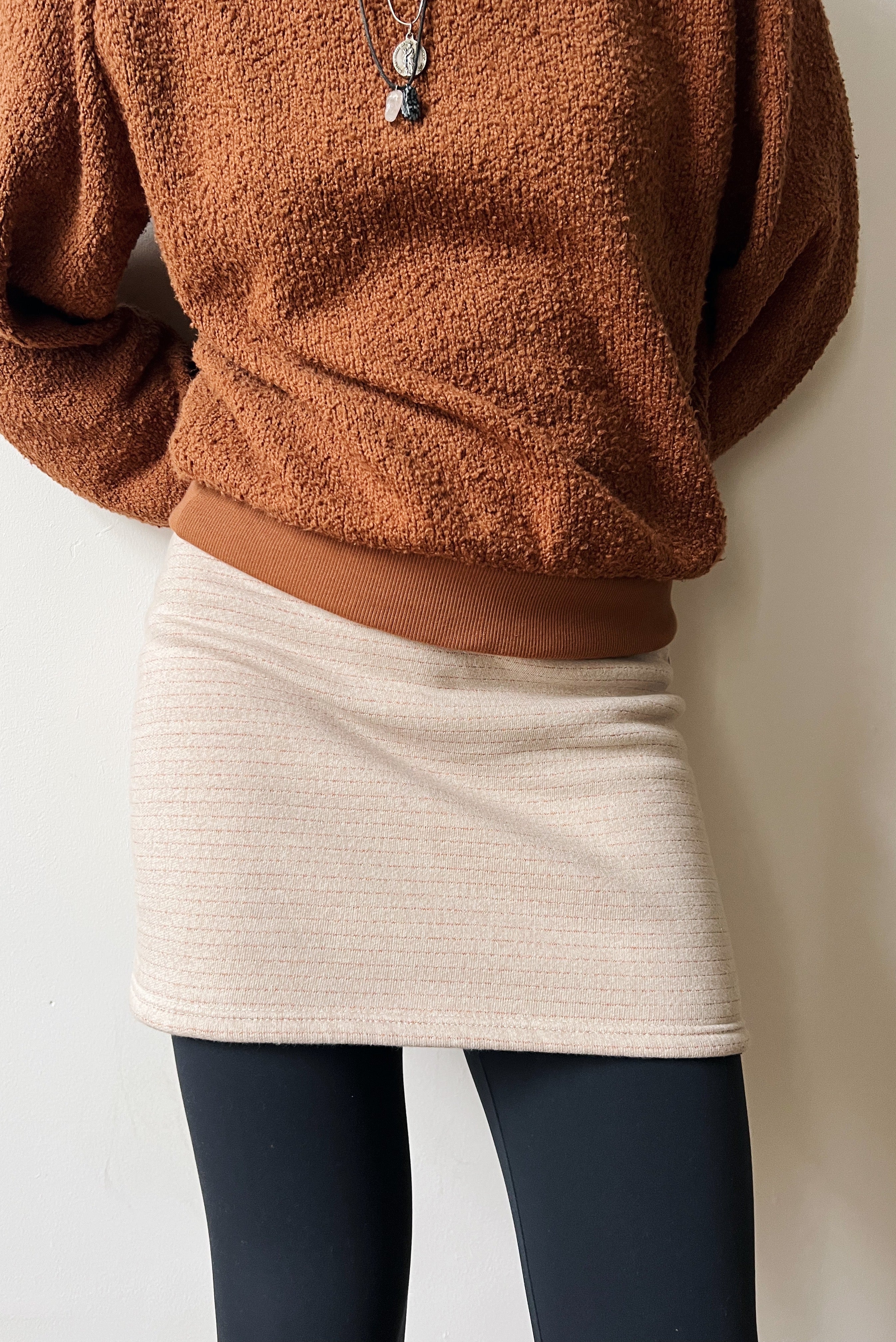 Person wearing a brown teddy sweater over a beige skirt with subtle bronze stripes with a neutral background