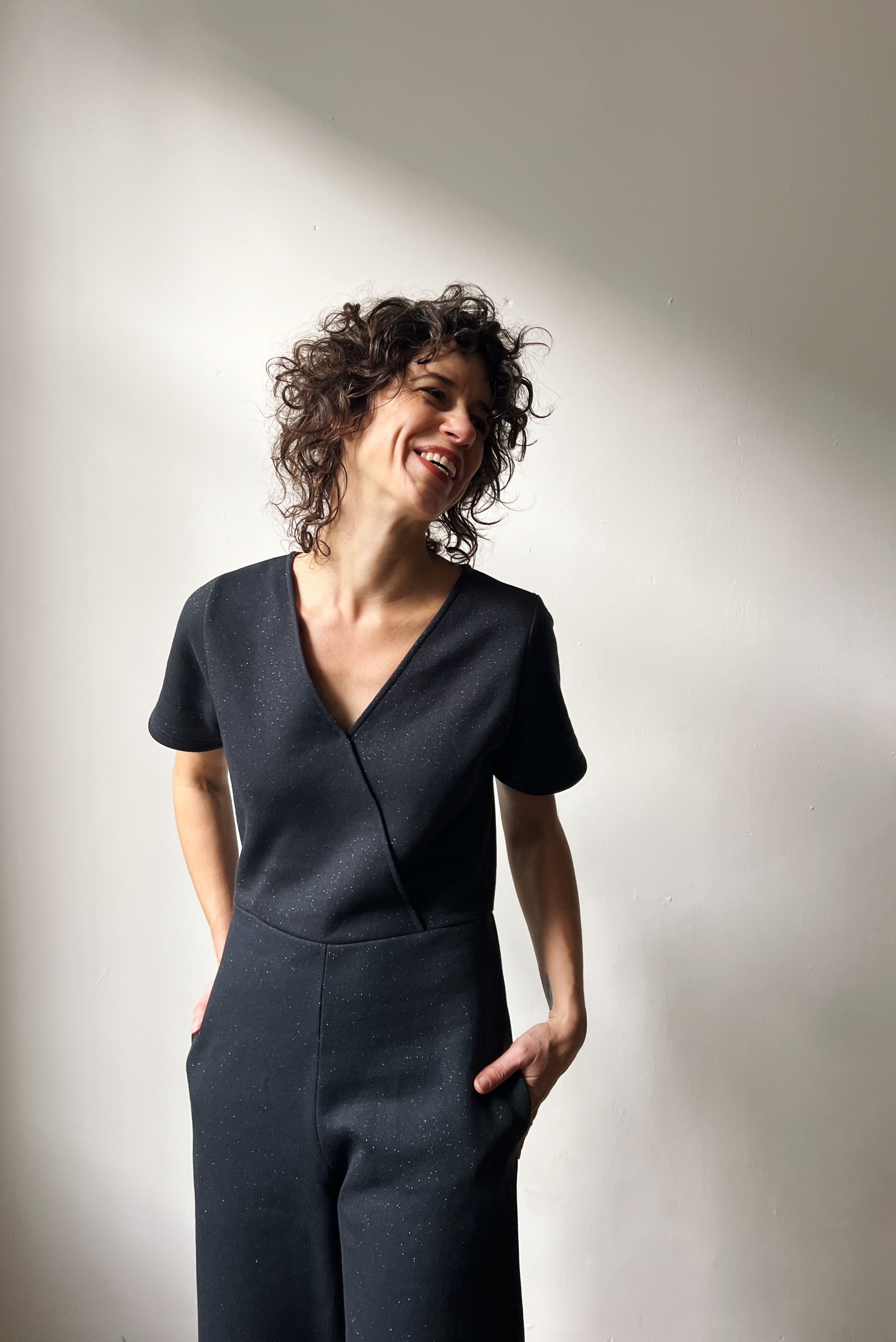 Woman wearing a dark gray sparkly jumpsuit with her hands in the pockets.