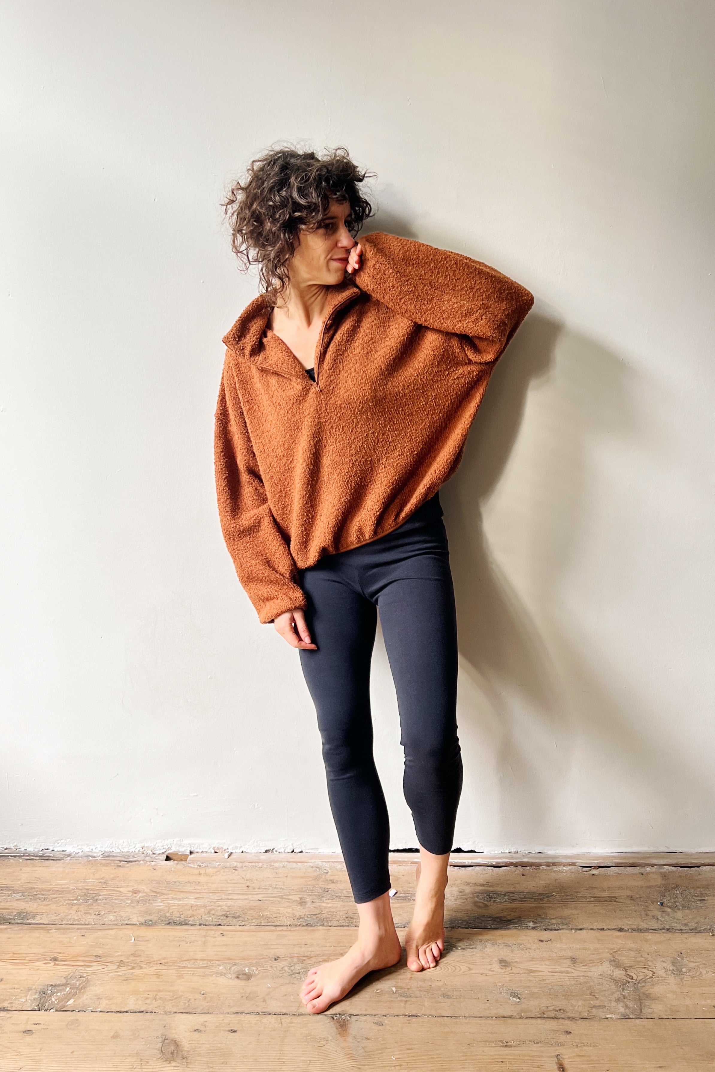 Person wearing a teddy brown sweater and black legging against a white wall.
