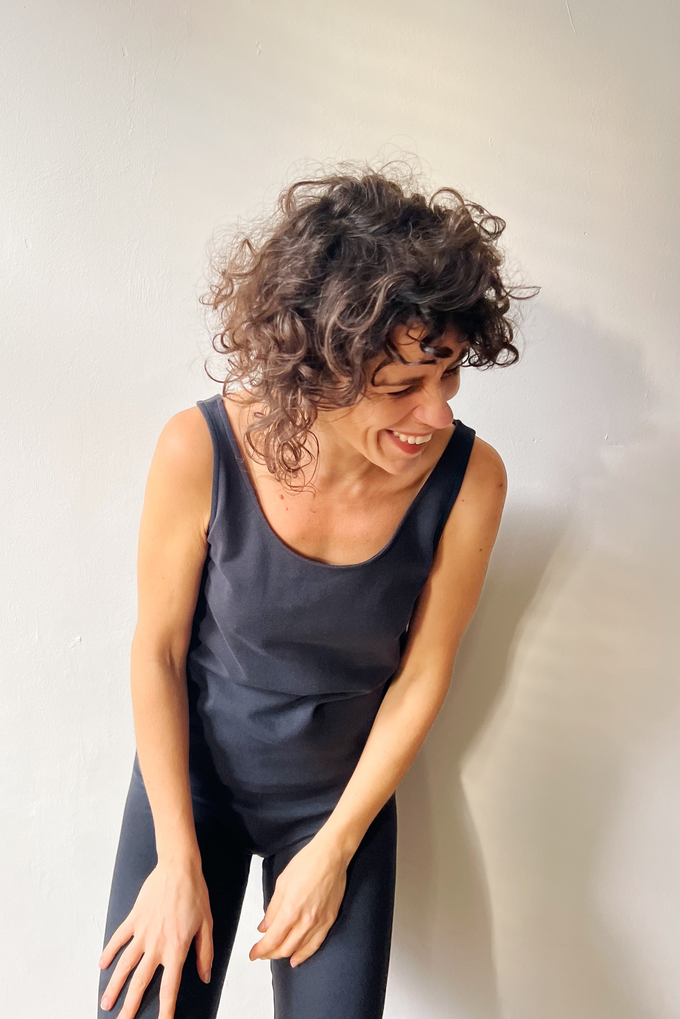 Woman in a dark sleeveless top and legging against a light background