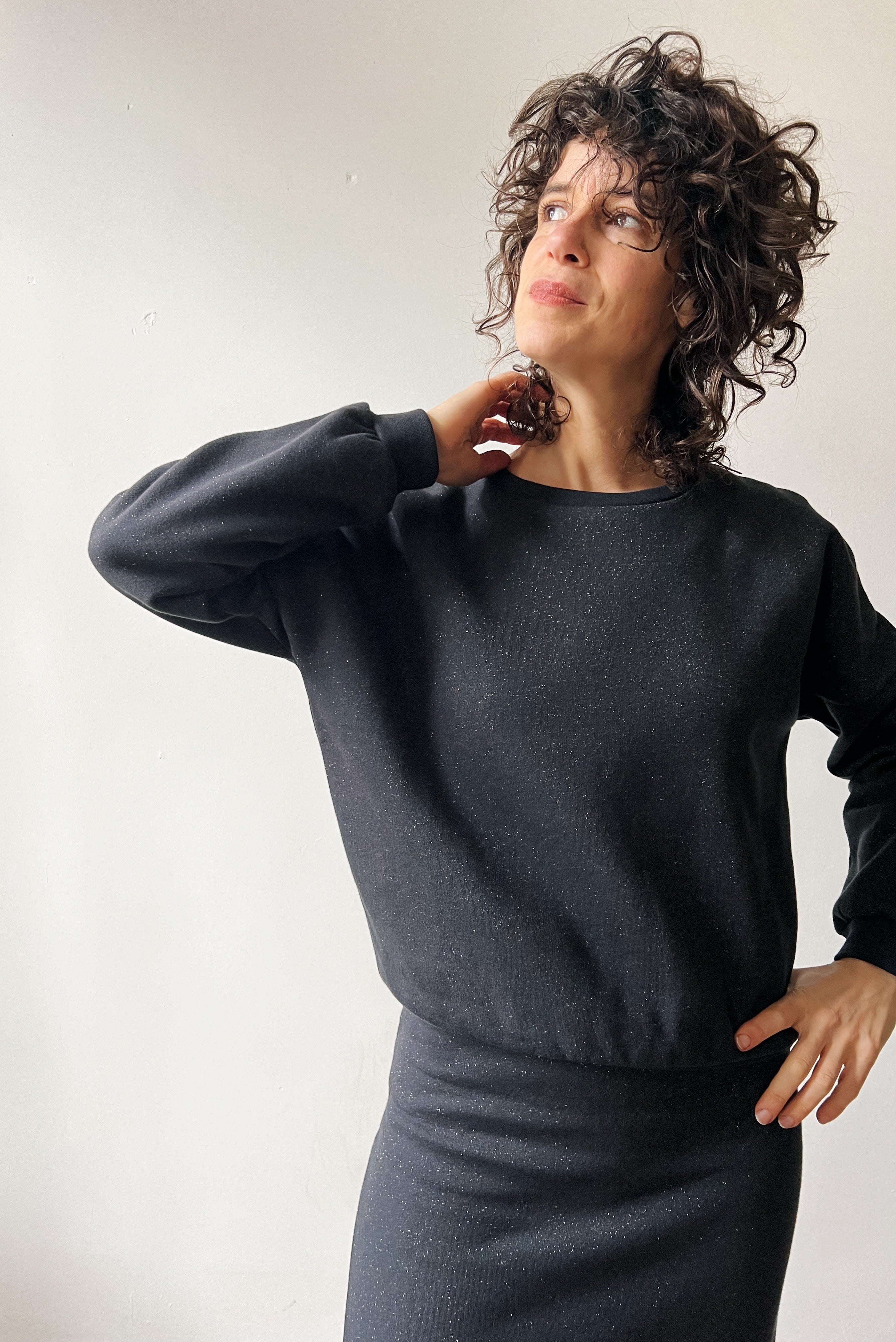 Woman wearing a dark gray sparkling sweater and skirt against a plain background