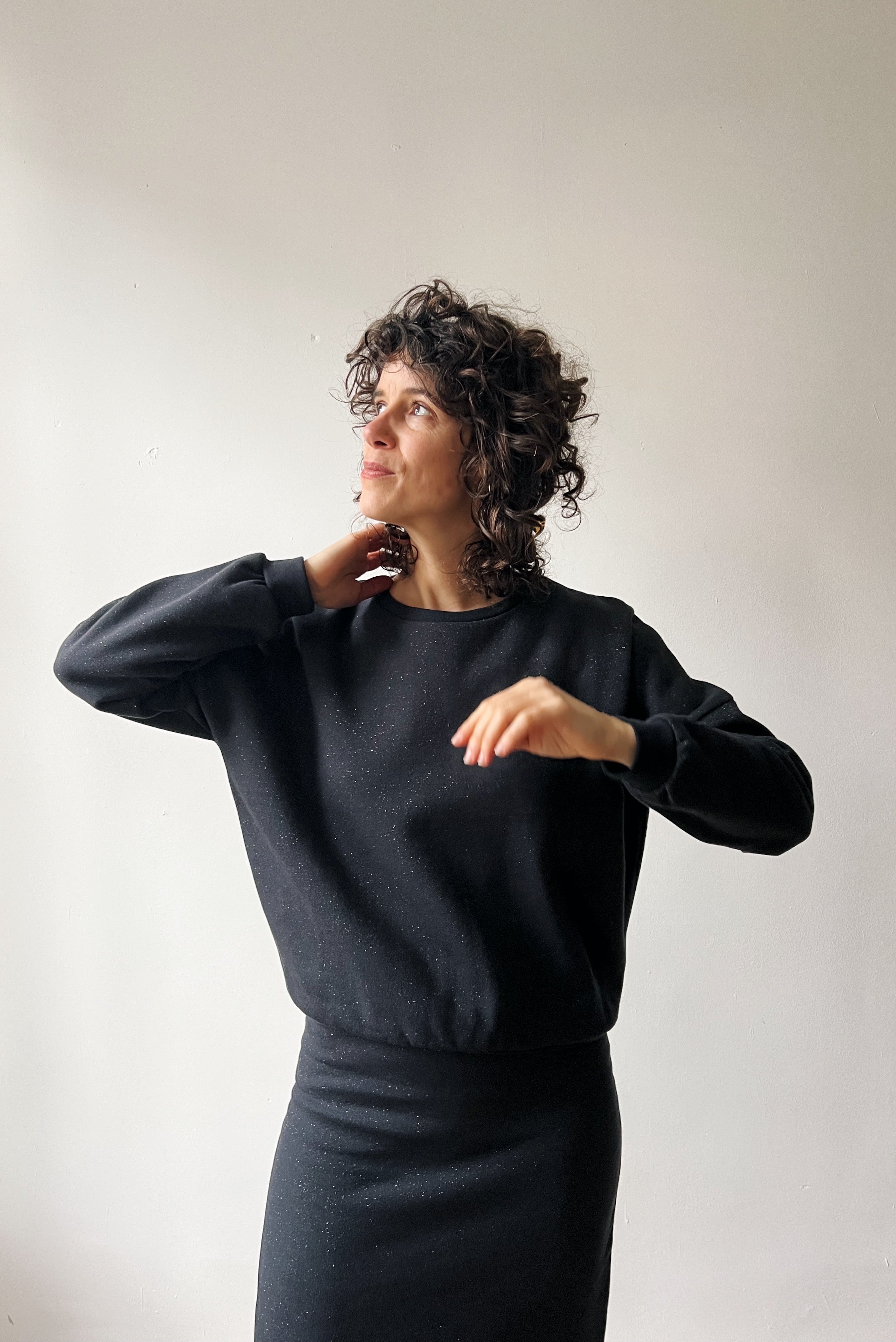 Woman wearing a dark gray sparkling sweater and skirt against a plain background