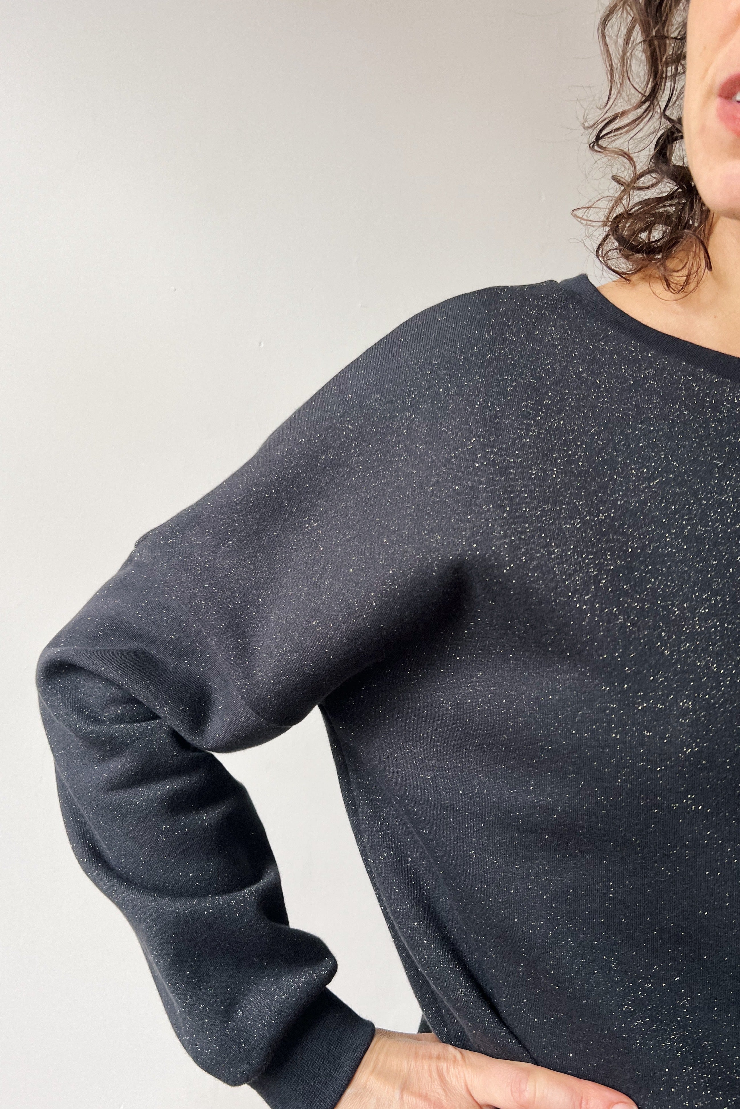 Person wearing a dark gray sparkling sweater against a plain background