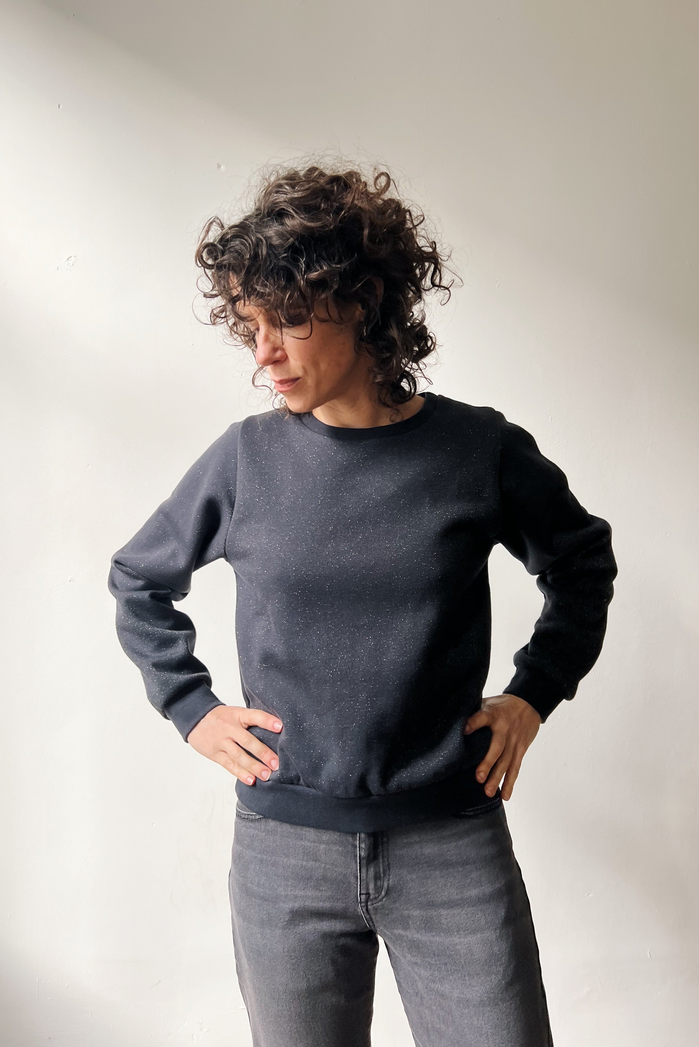 Person wearing a subtle sparking dark gray sweater and gray jeans against a plain background