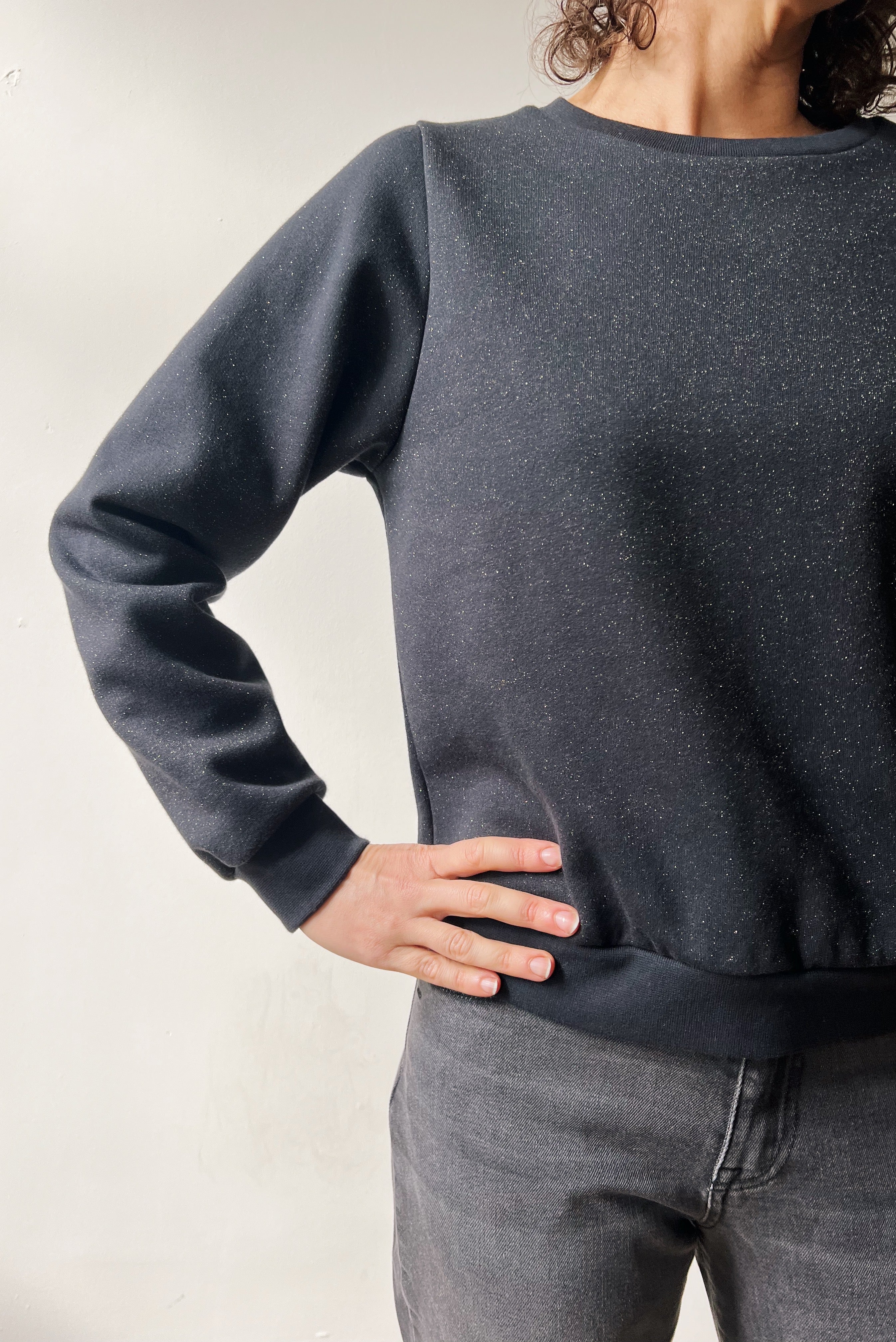 Person wearing a dark gray sweatshirt and jeans against a plain background