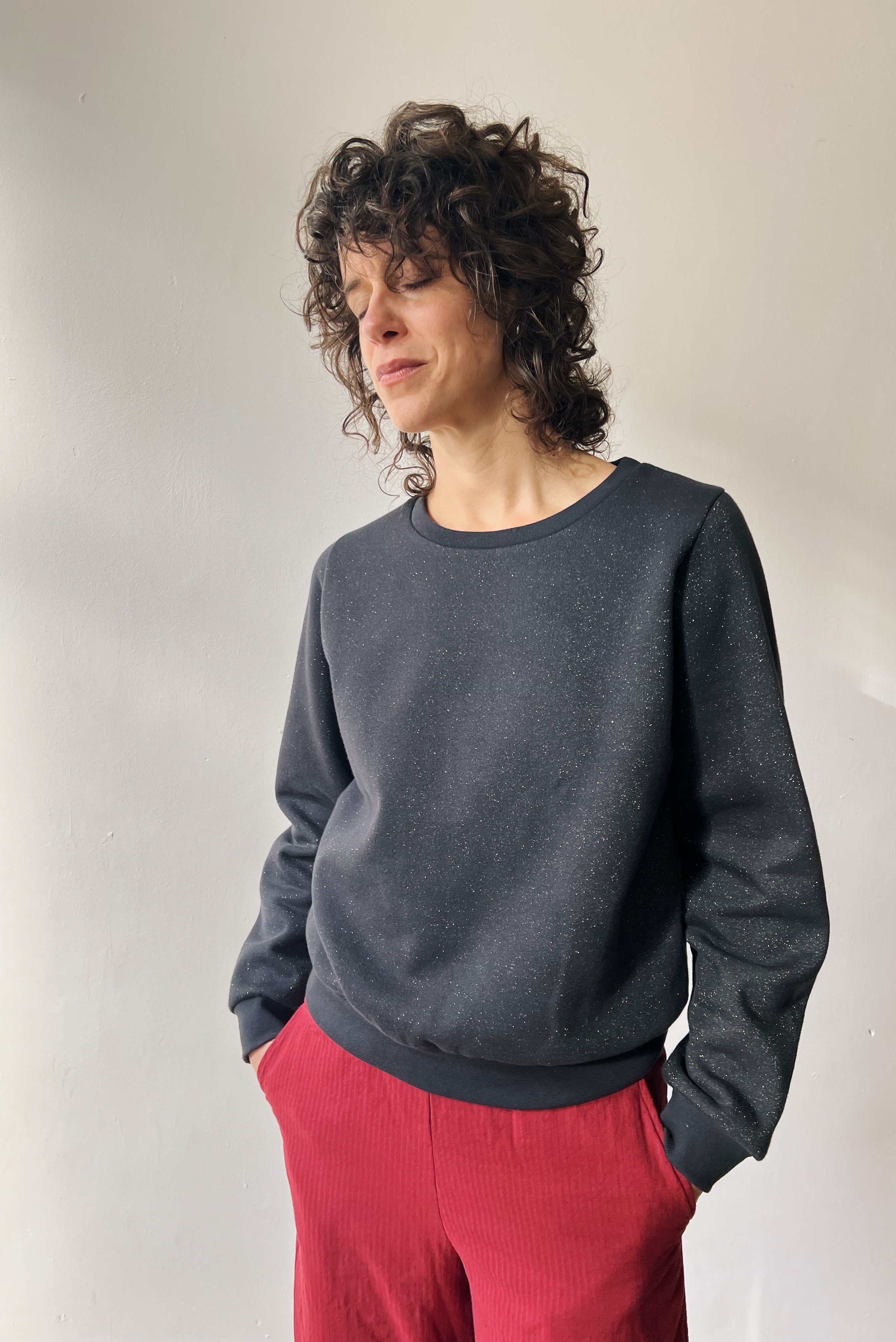 Person wearing a subtle sparking dark gray sweater and red corduroy pants against a plain background
