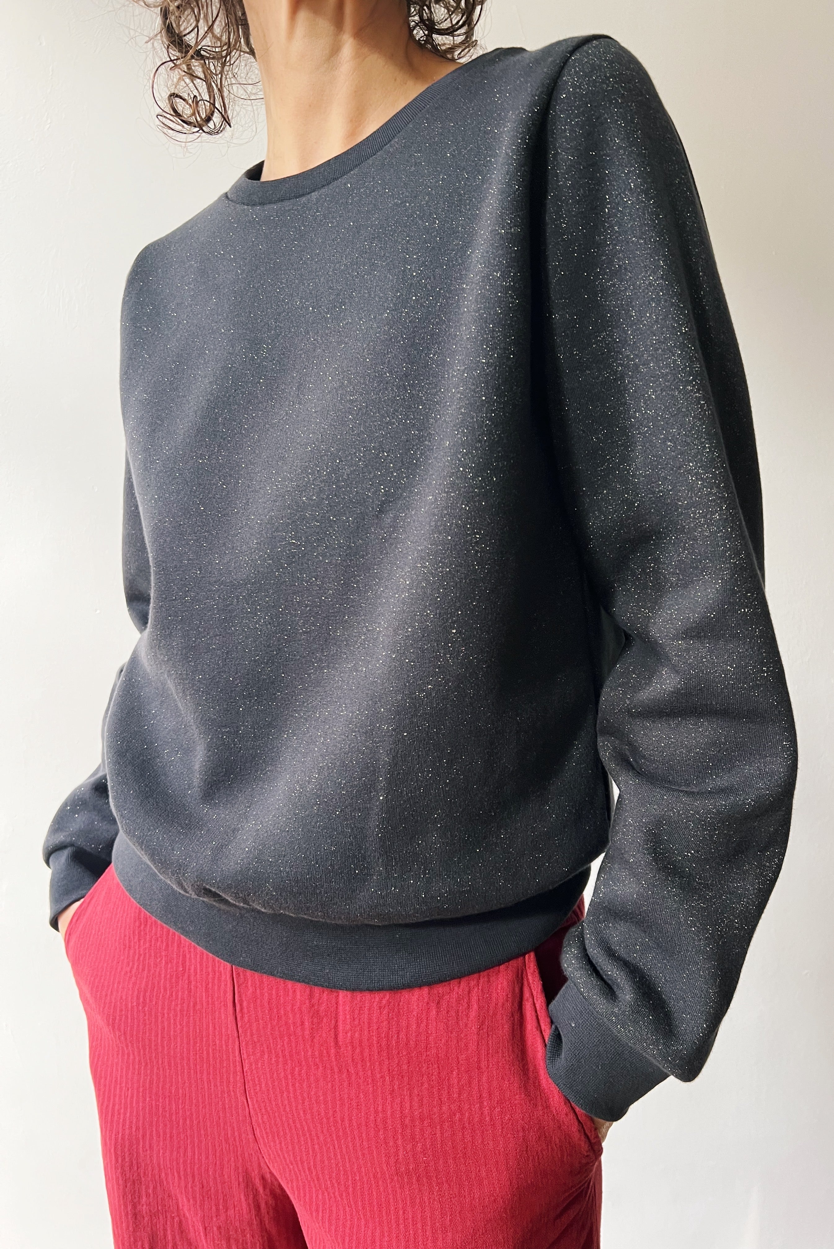 Person wearing a subtle sparking dark gray sweater and red corduroy pants against a plain background