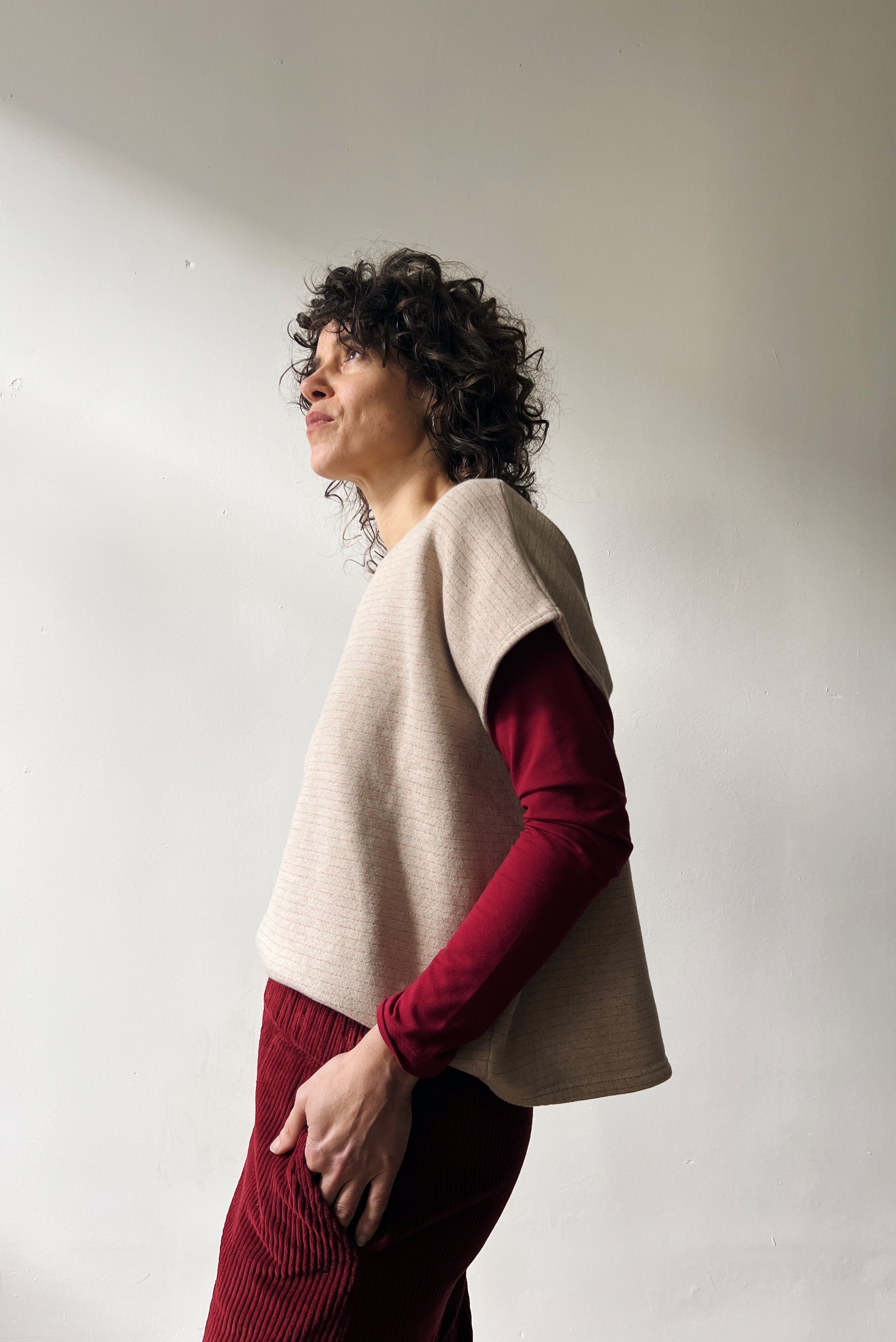 Woman wearing a beige shortsleeve sweater, red longsleeve and red pants standing against a white wall.