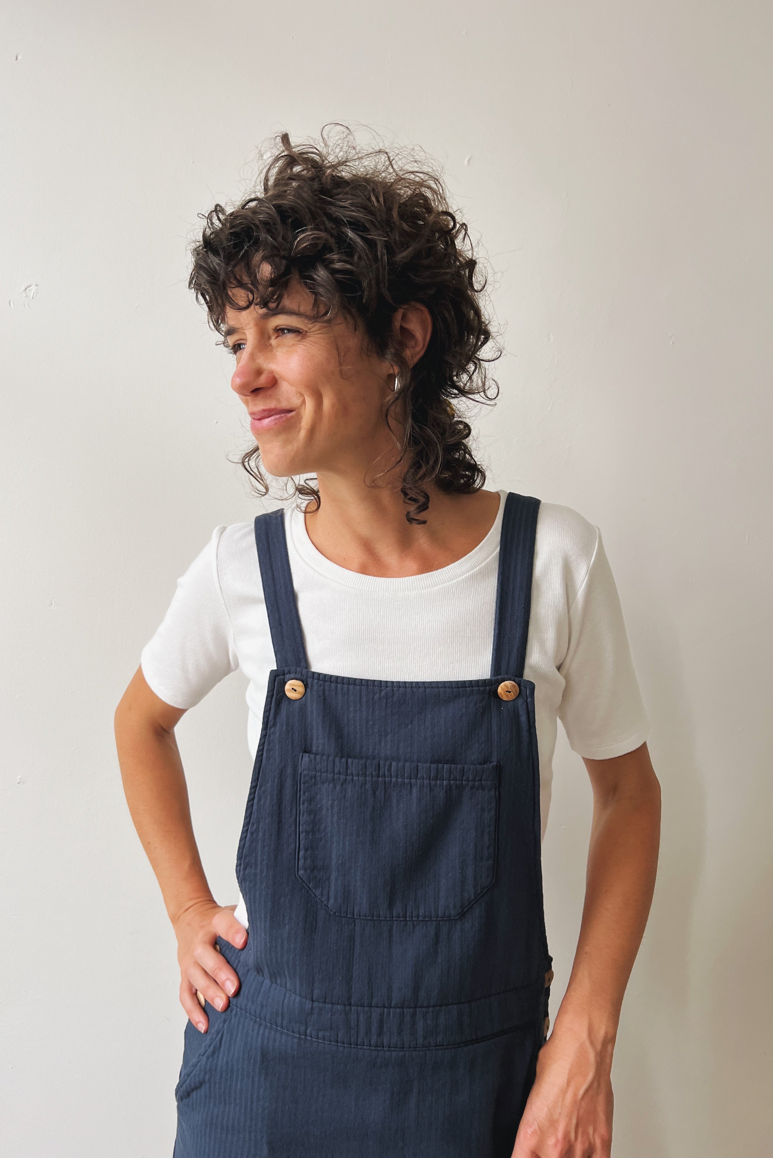 Person wearing a white shirt and blue corduroy salopettedress against a plain background