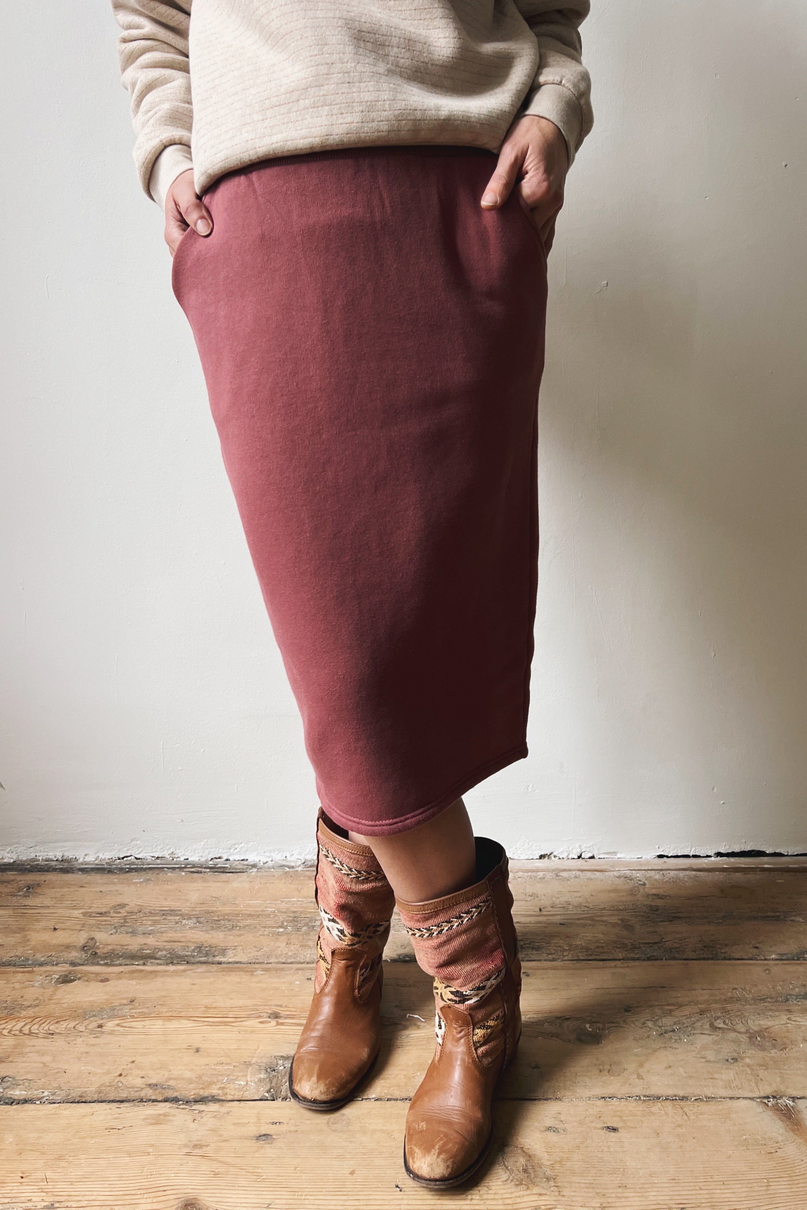 Person wearing a figue skirt and brown boots on a wooden floor with a white wall background