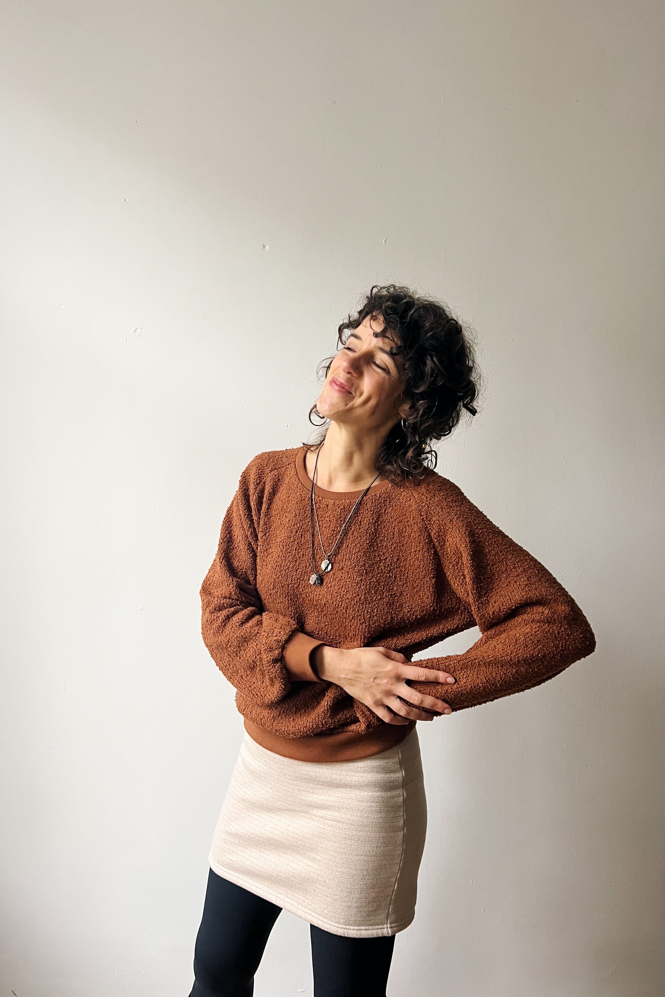 Woman wearing a brown sweater and beige skirt against a plain background