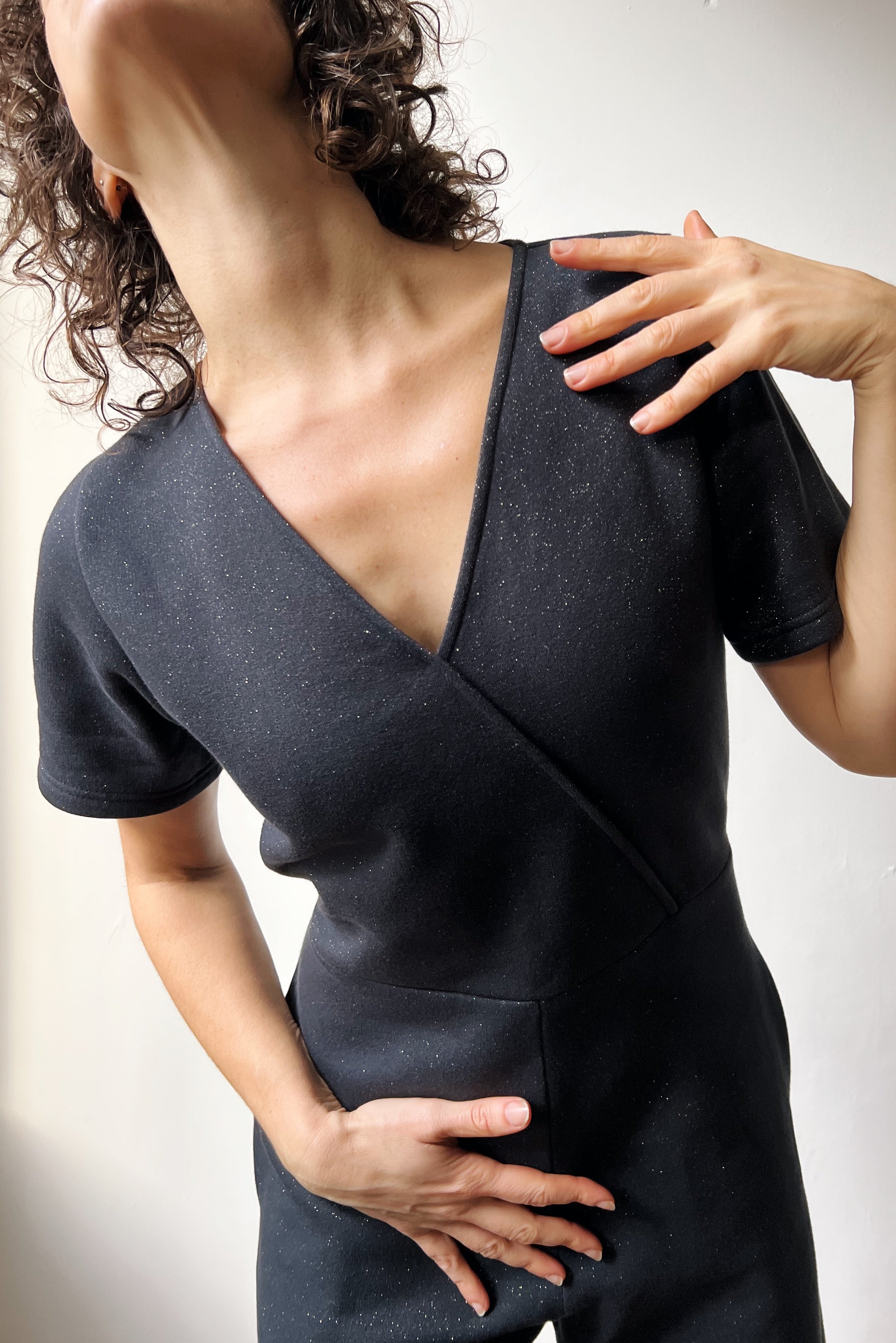 Woman wearing a dark gray sparkly jumpsuit with a unique cutout design on a plain background