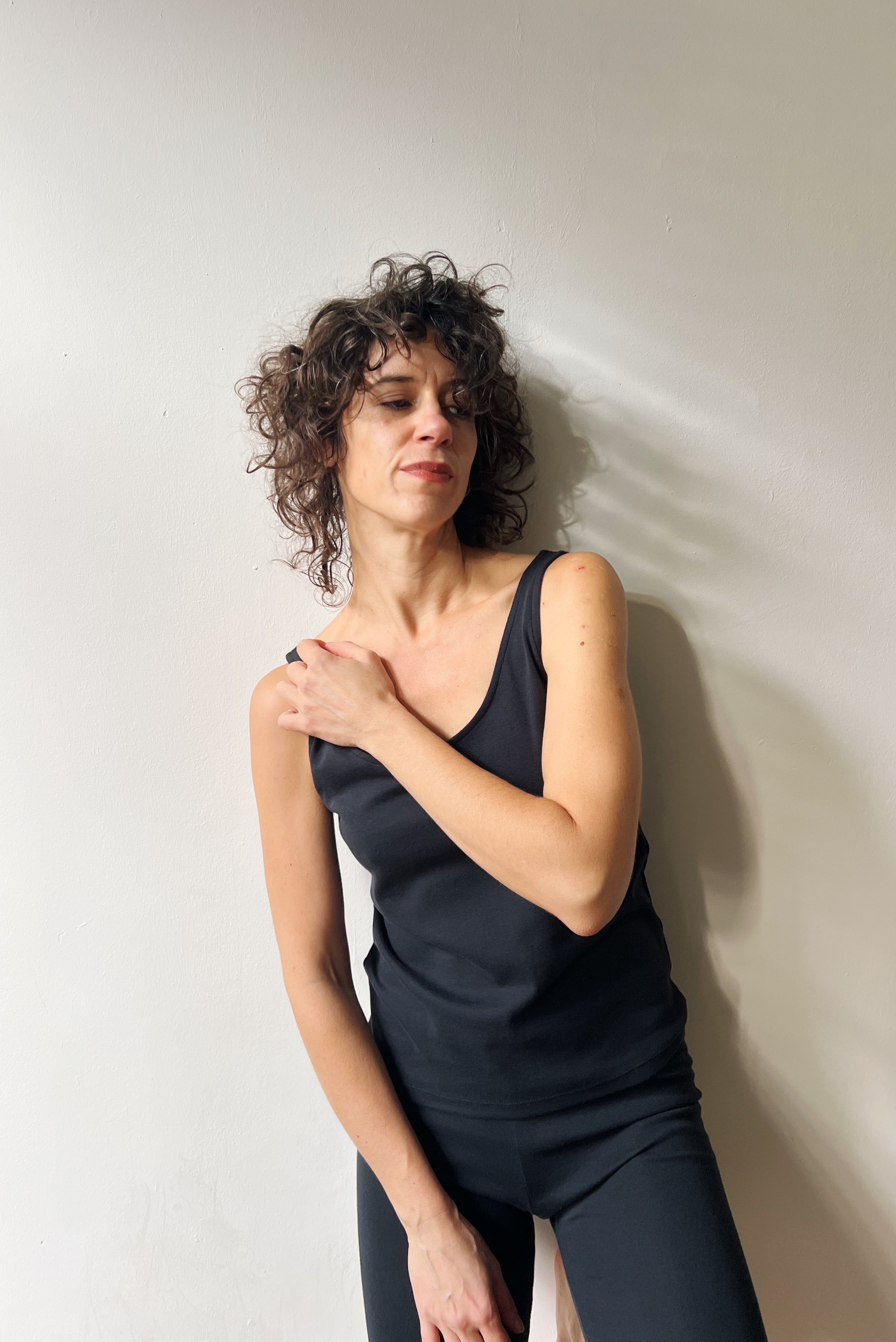 Woman in a black sleeveless top and leggings against a white wall