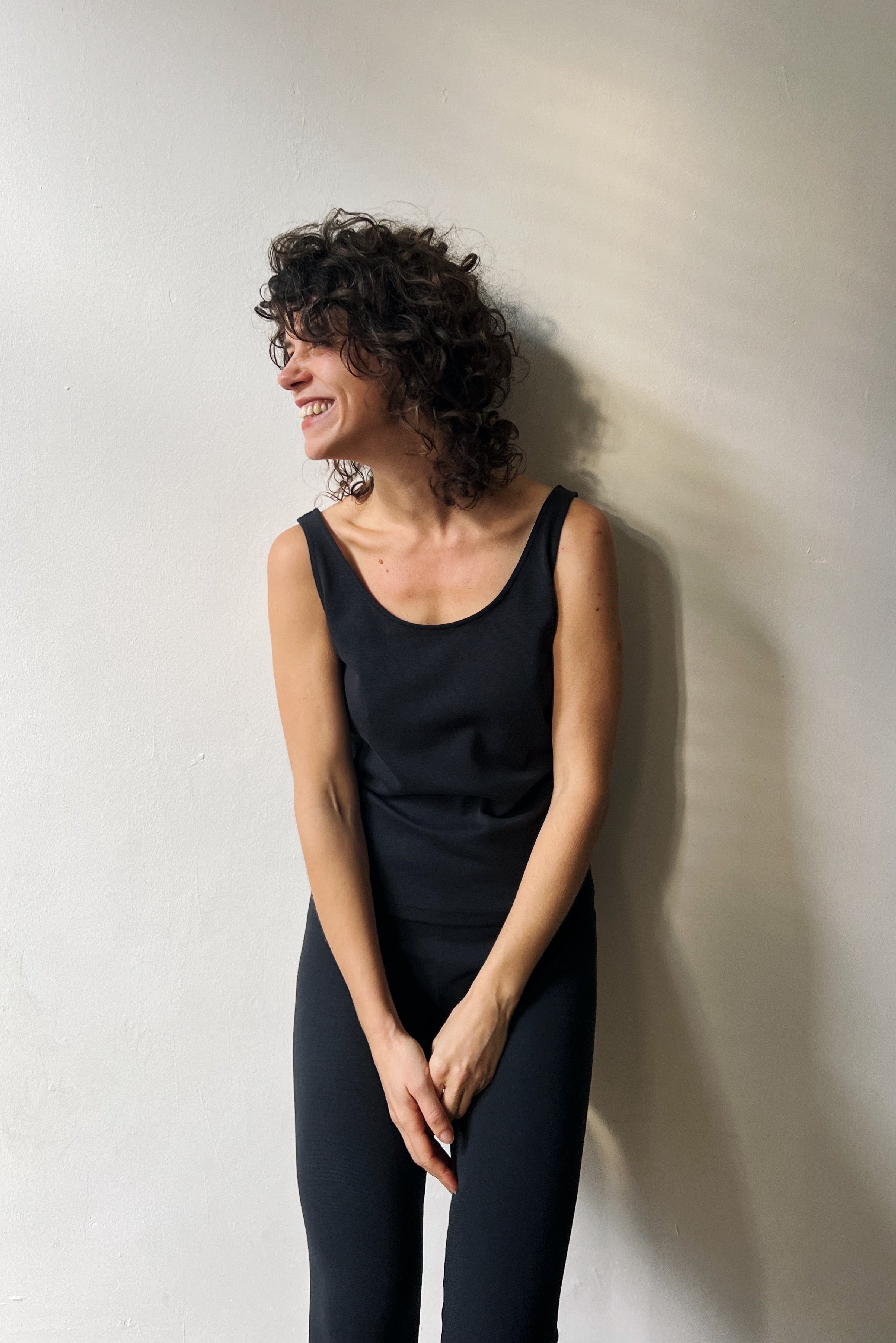 Woman in a black sleeveless top and leggings against a white wall