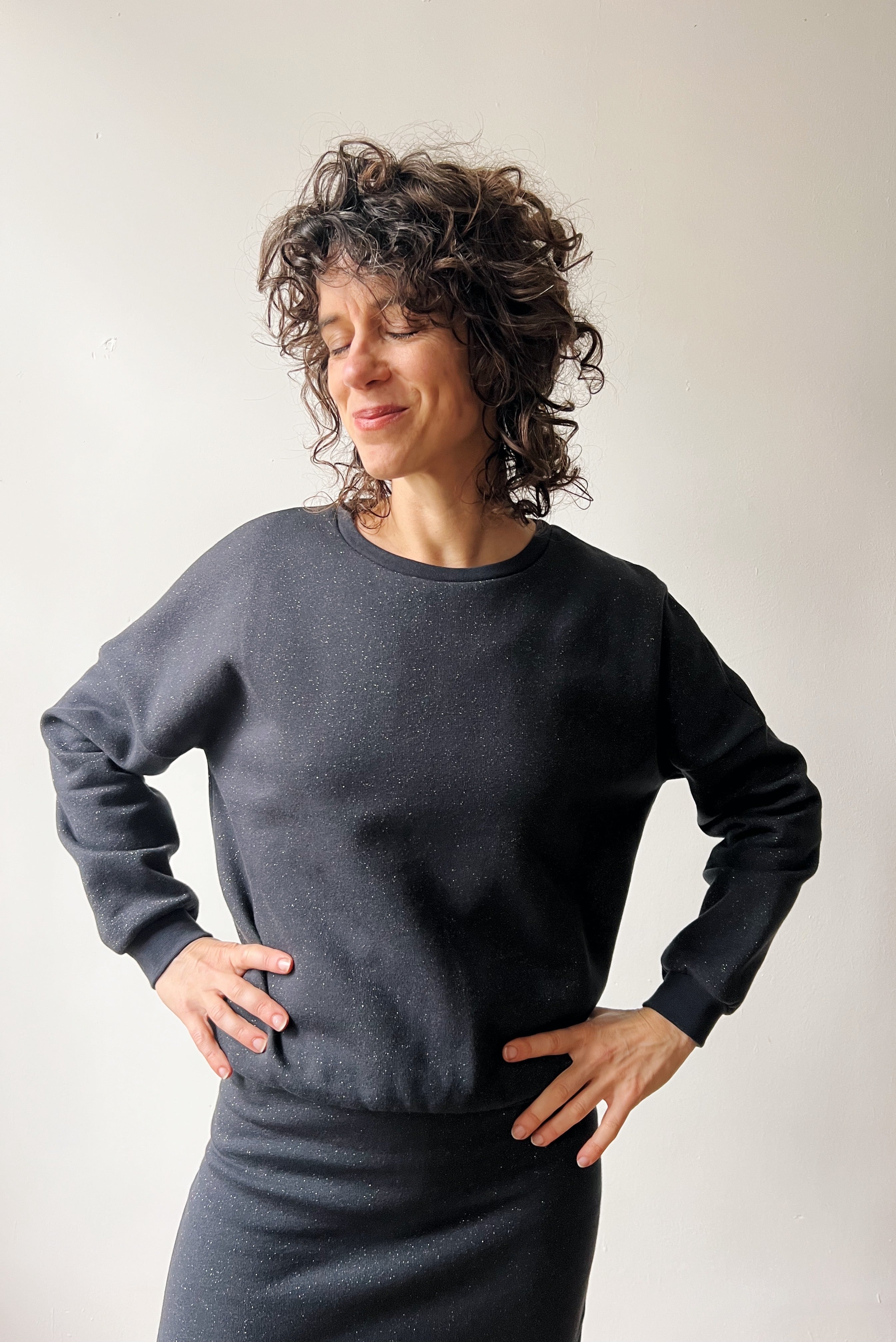 Woman wearing a dark gray sparkling sweater and skirt against a plain background