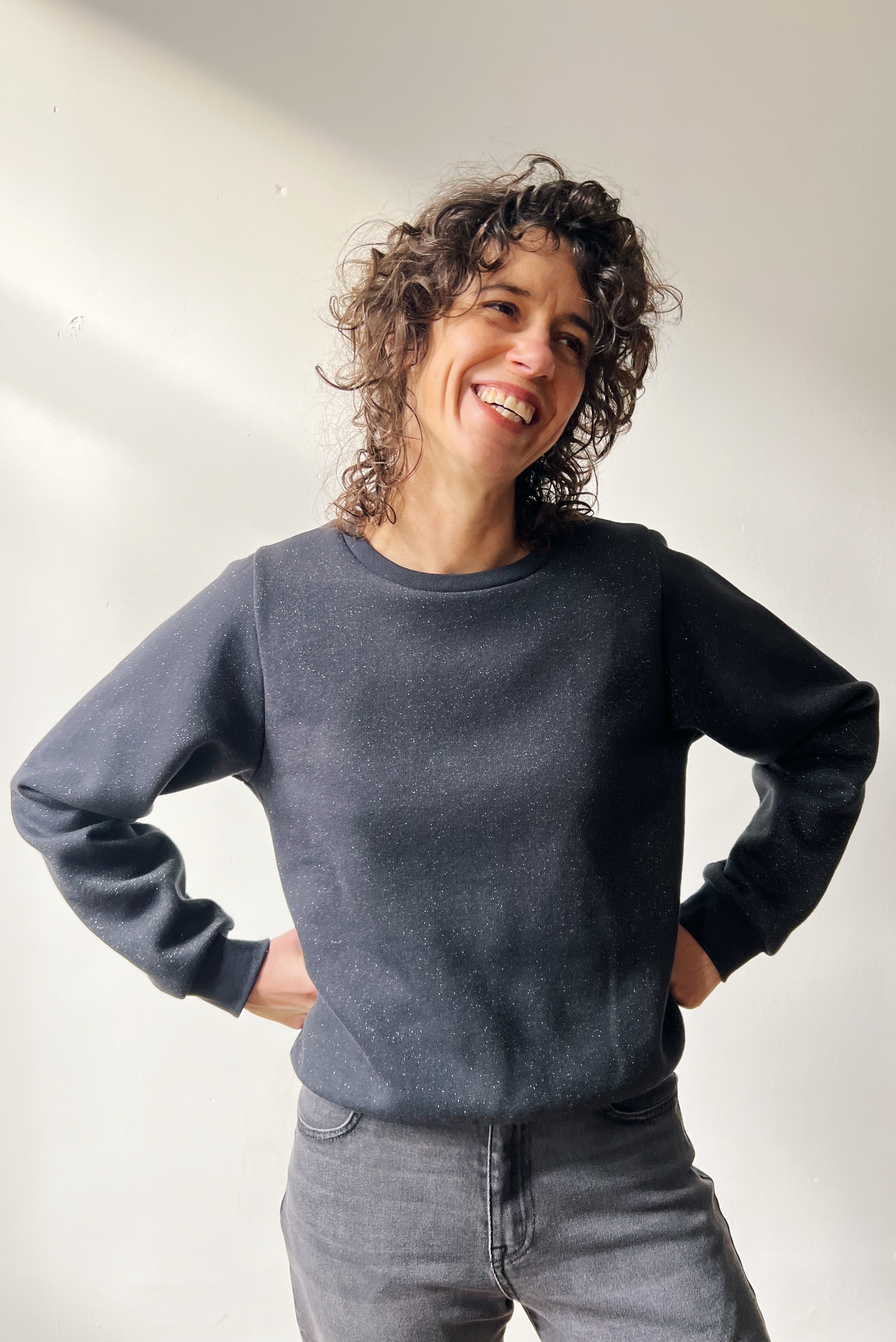 Person wearing a subtle sparking dark gray sweater and gray jeans against a plain background