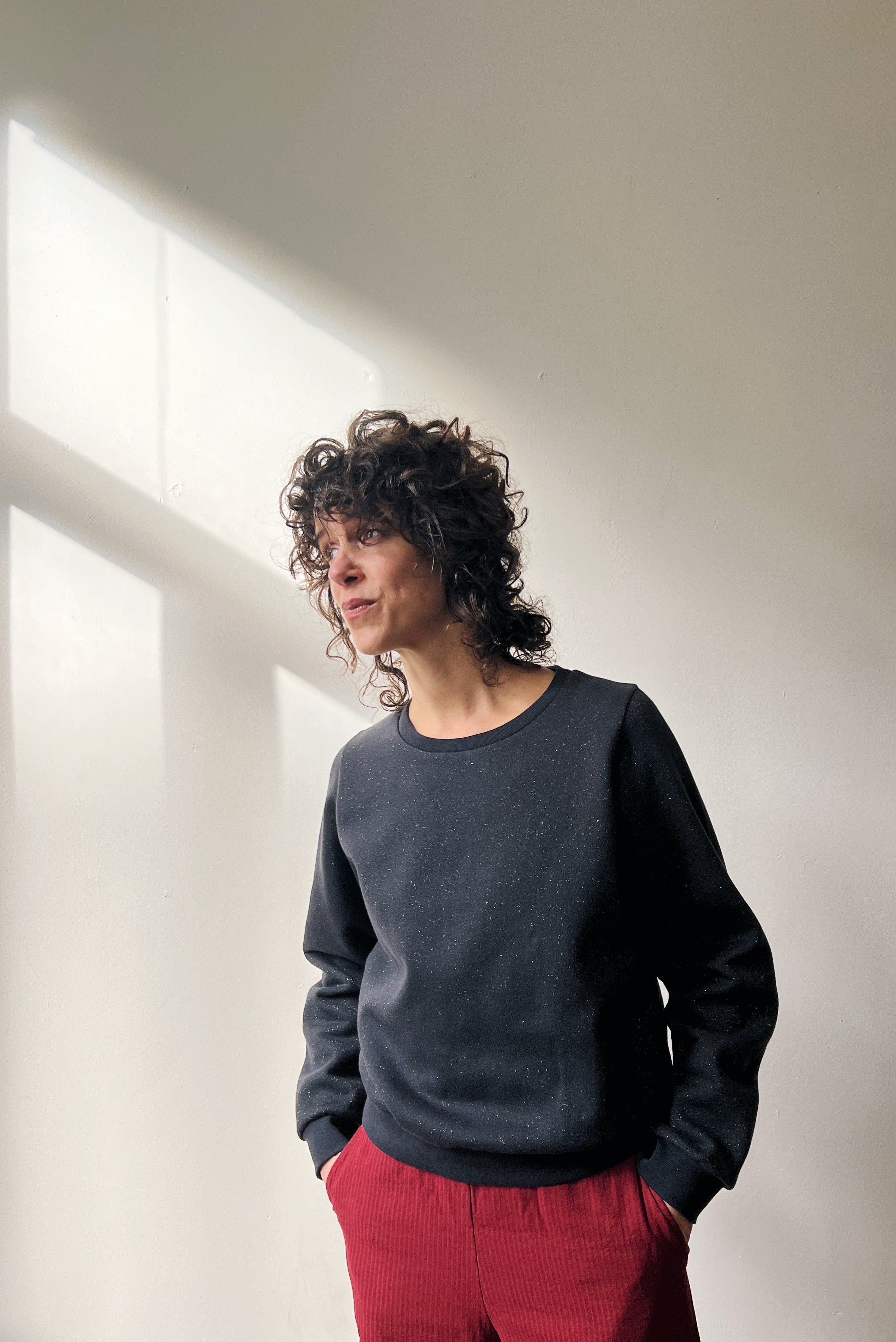 Person wearing a subtle sparking dark gray sweater and red corduroy pants against a plain background