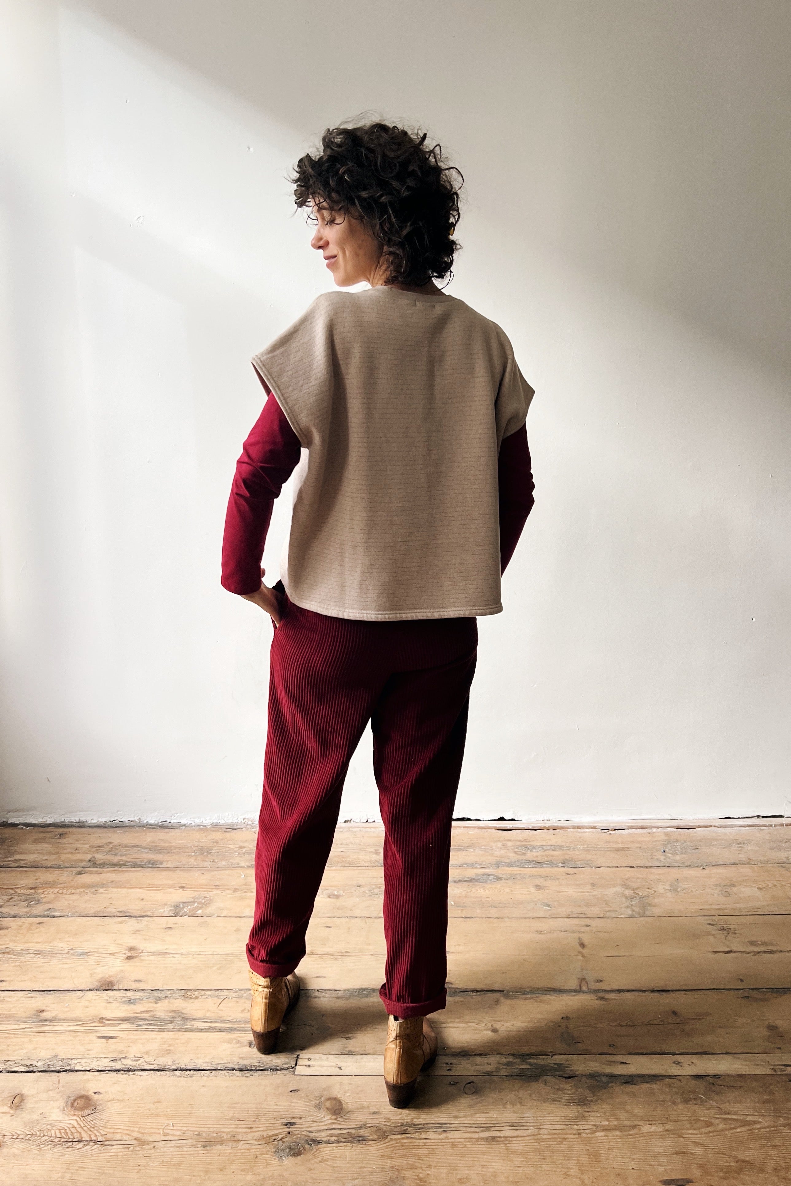 Woman wearing a beige shortsleeve sweater, red longsleeve and red pants standing against a white wall.