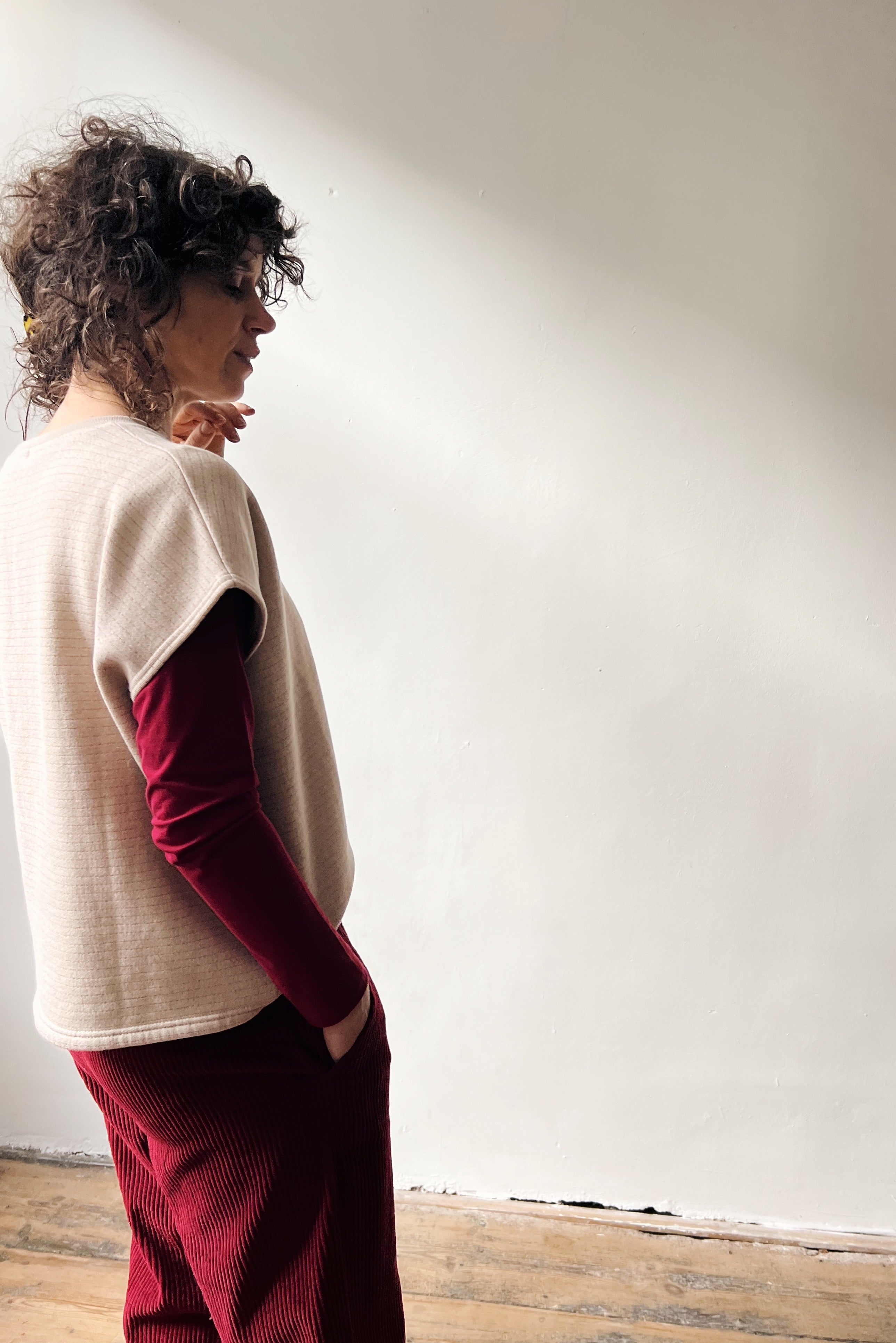 Woman wearing a beige shortsleeve sweater, red longsleeve and red pants standing against a white wall.
