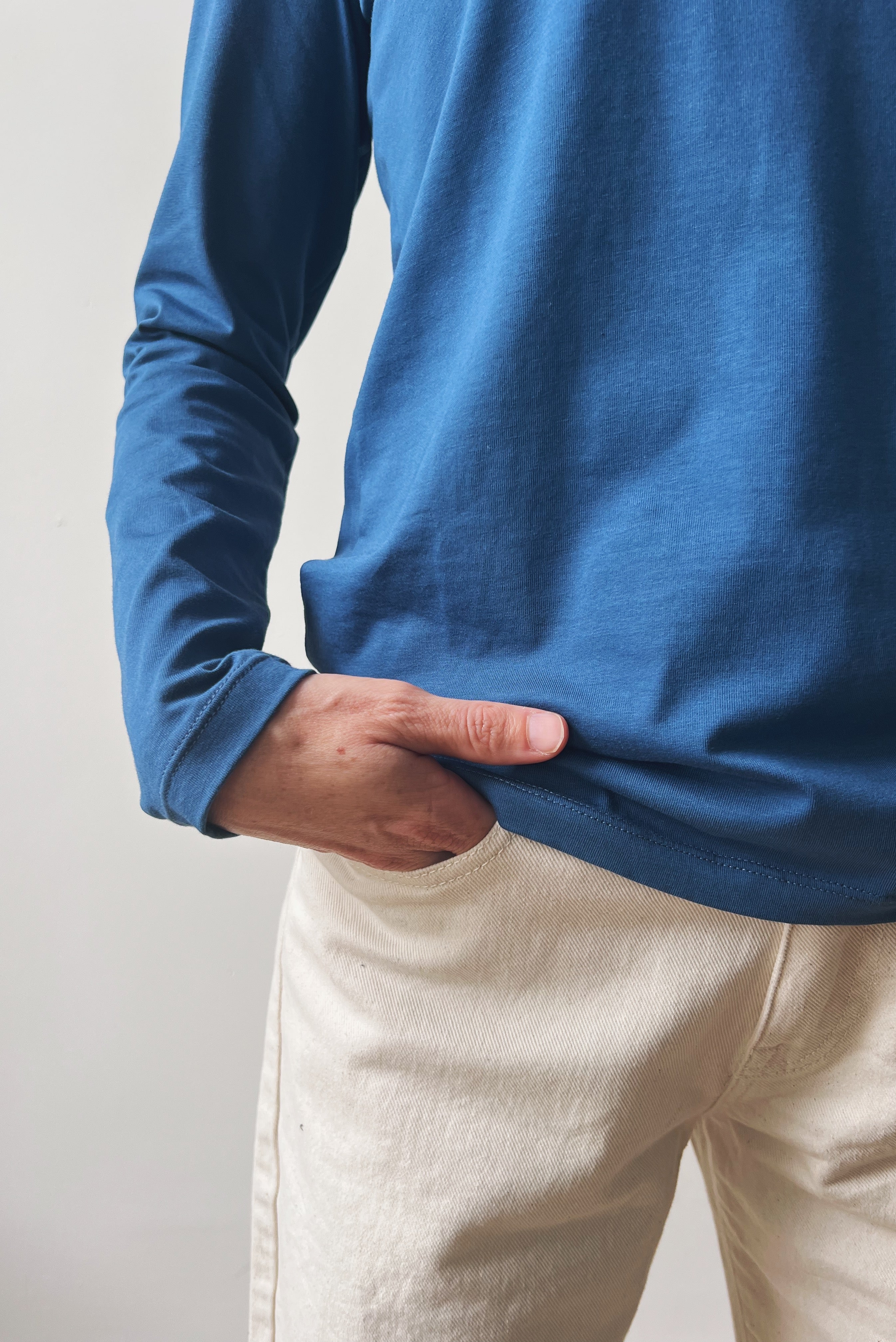 Close-up of a person wearing a blue long-sleeve shirt and oat boyfriend jeans against a plain background