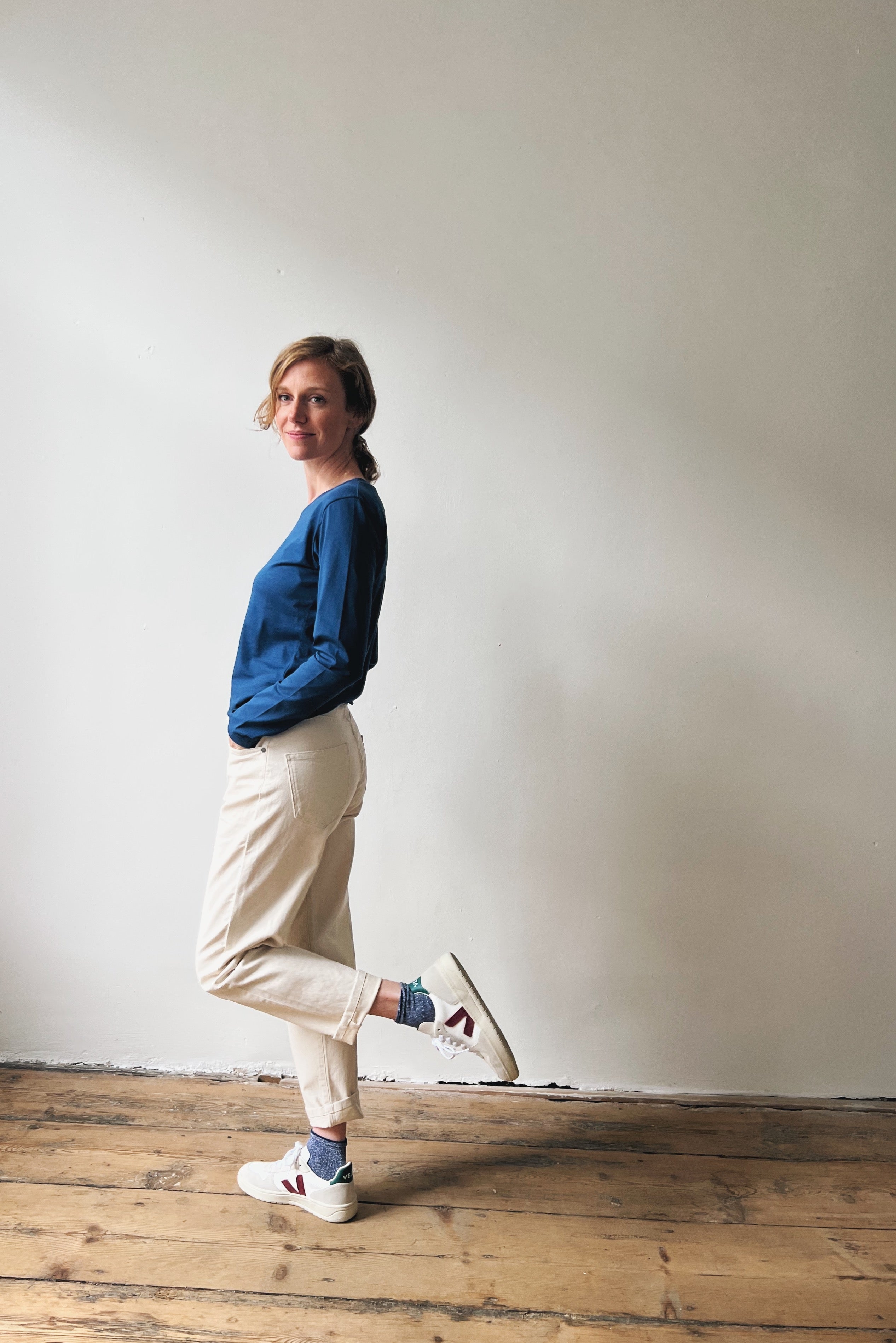 Person wearing a blue sweater and beige pants standing against a plain wall.